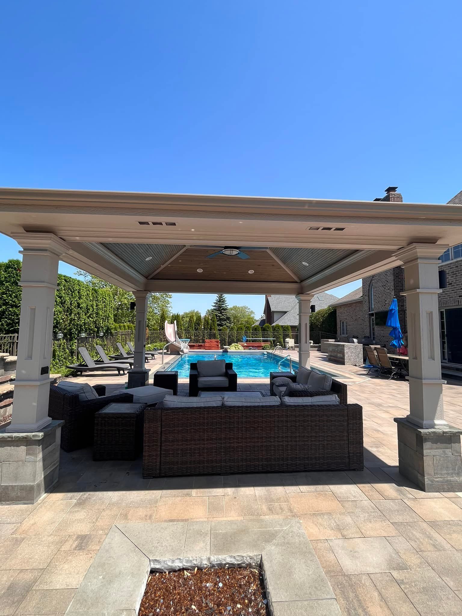 A gazebo with a couch and chairs in front of a pool.