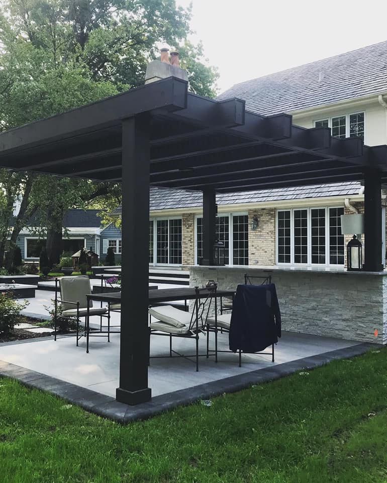 A patio with a table and chairs under a pergola in front of a house.