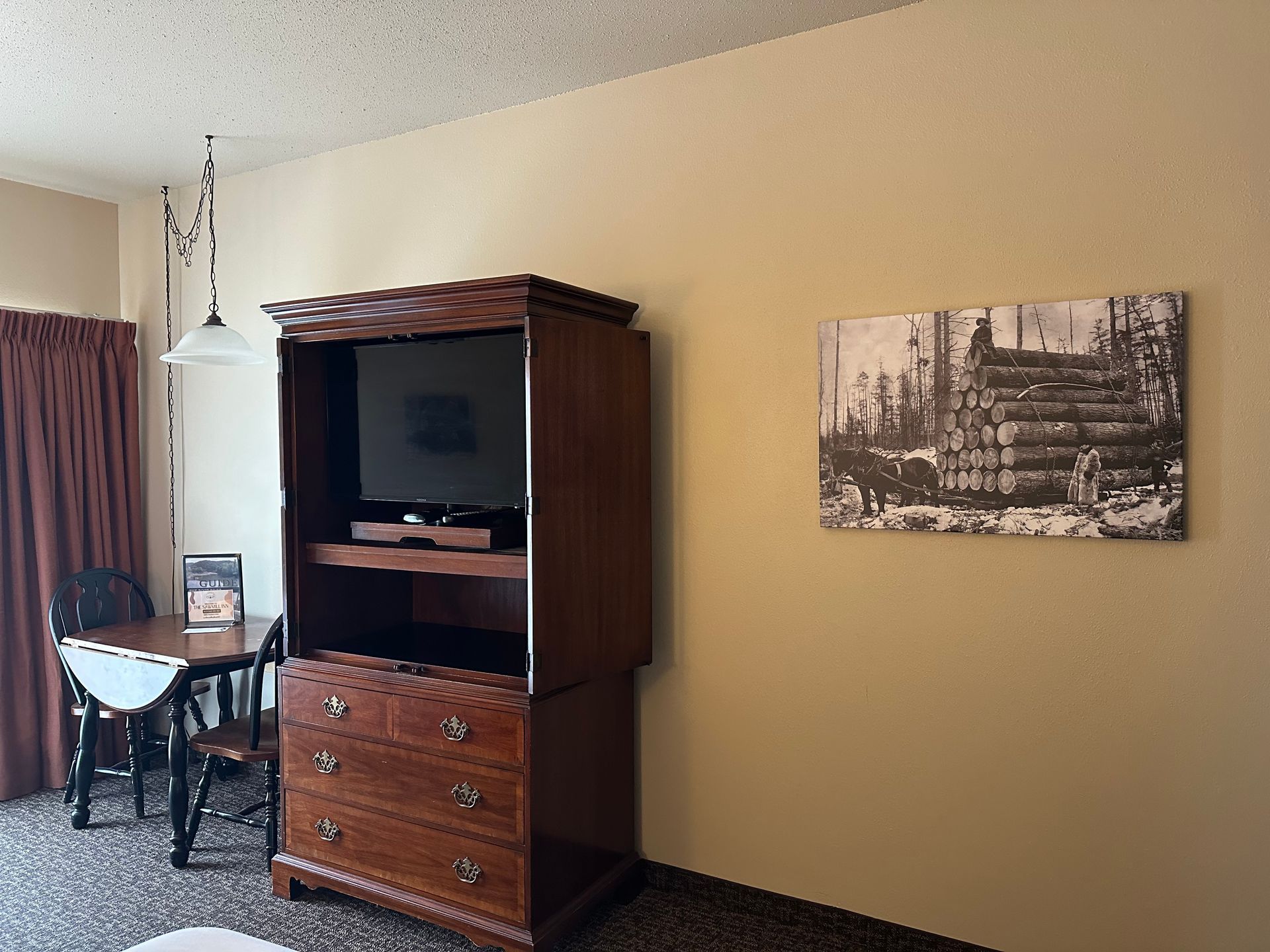 Hotel room with wooden cabinet holding a TV. A small table and chairs sit beside a dark curtain.