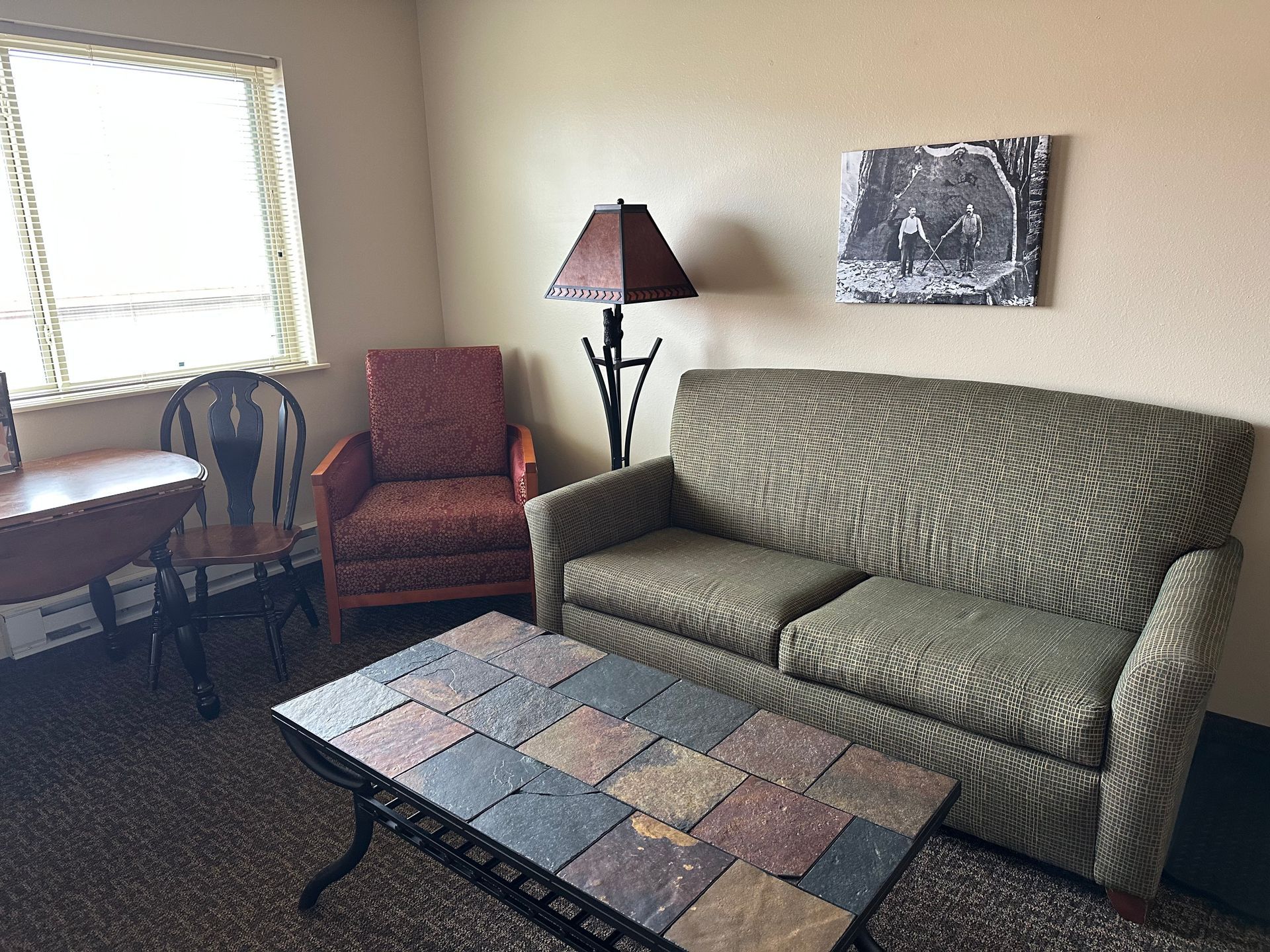 Living room with a green sofa, red armchair, and tile-topped coffee table. A window, desk, and lamp are also visible.