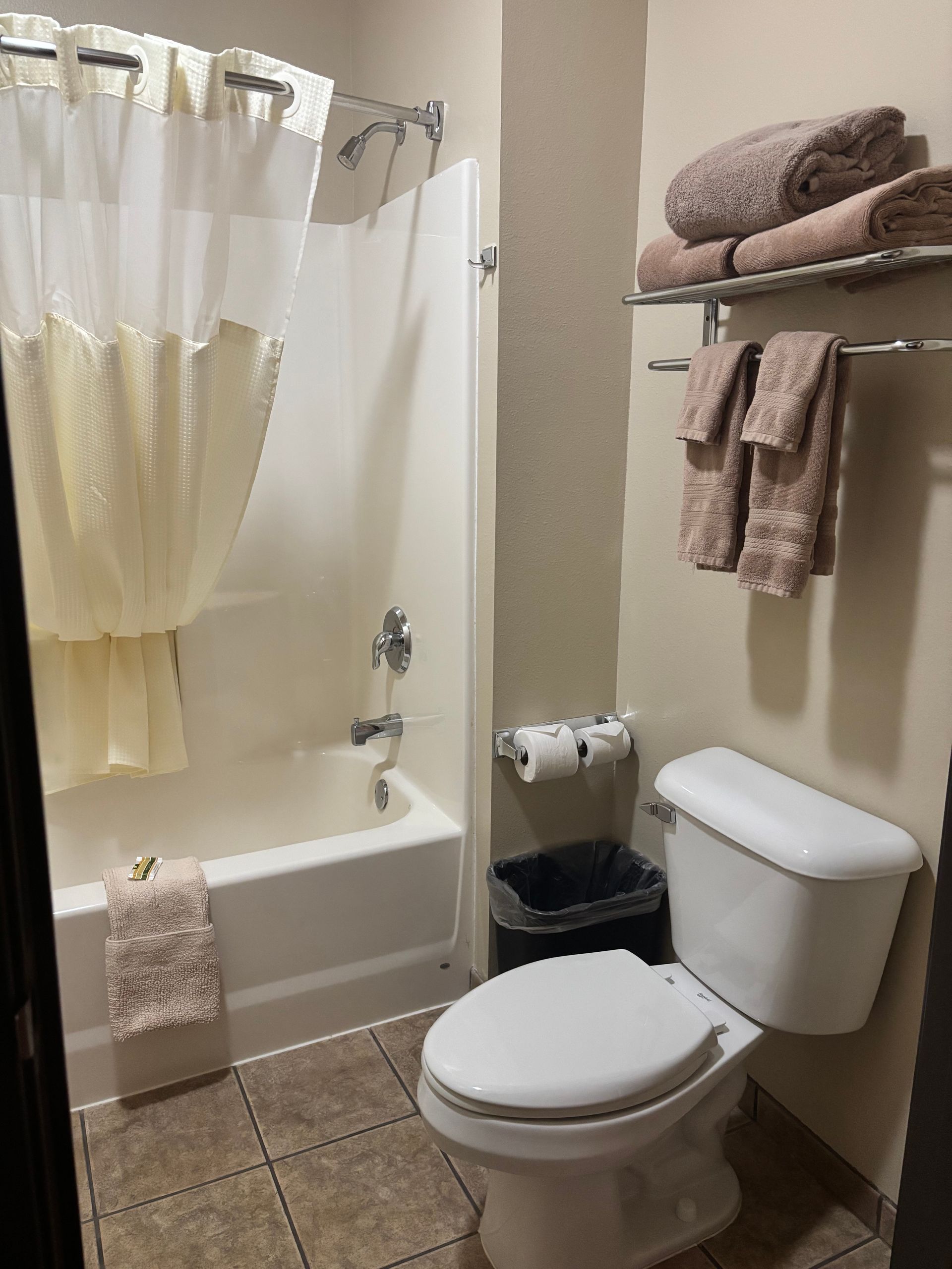 Bathroom with a white bathtub, toilet, and tan towels. Brown tile floor.