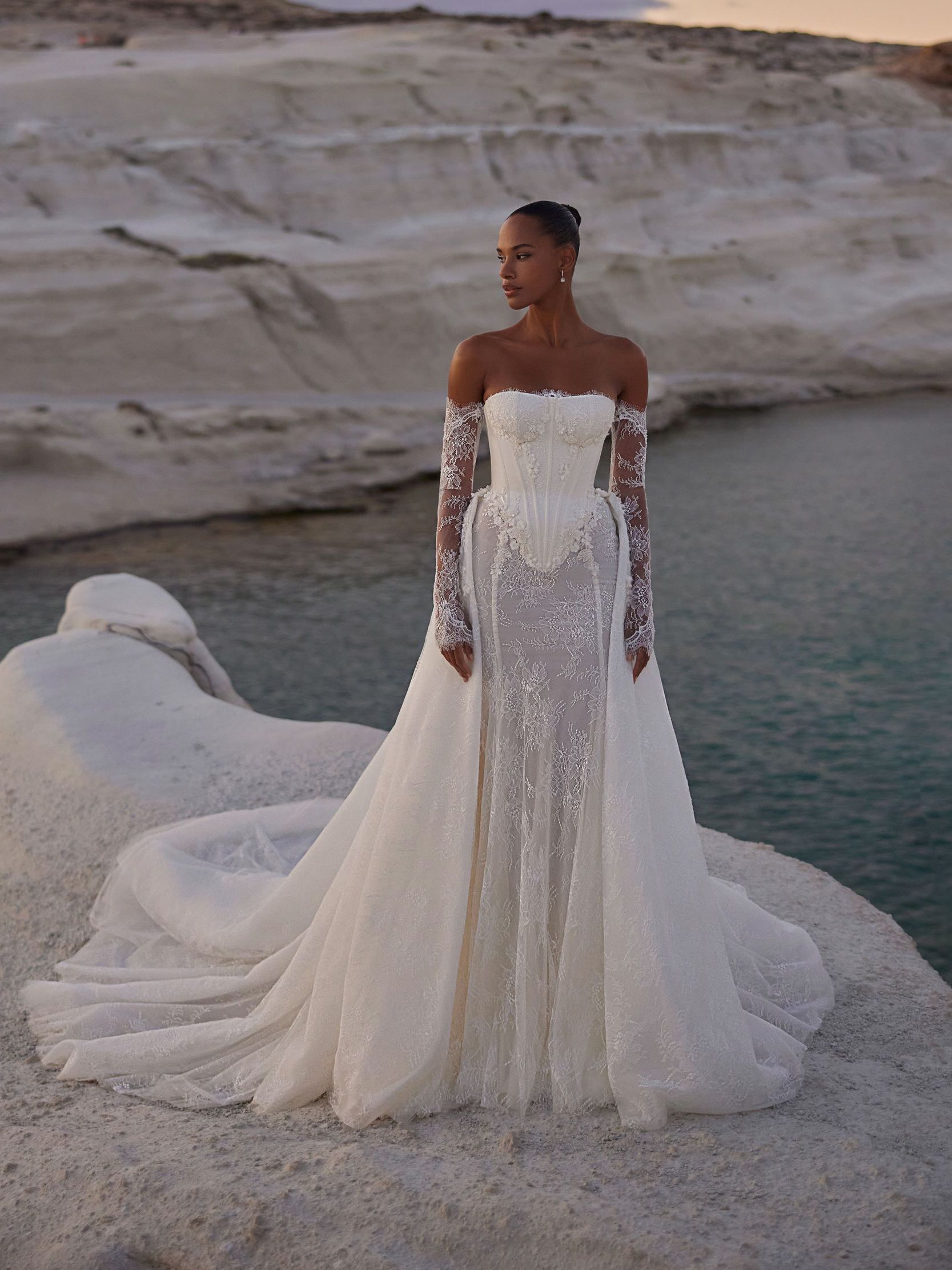 A black and white photo of a woman in a wedding dress standing next to a body of water.