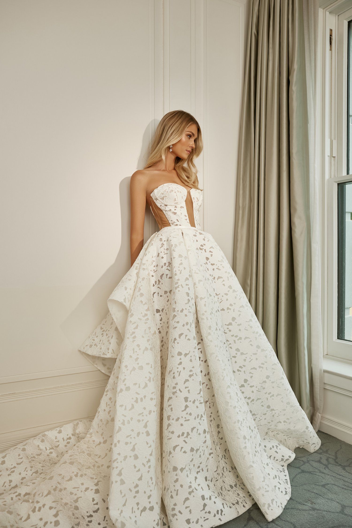 A woman in a wedding dress is standing in front of a window.