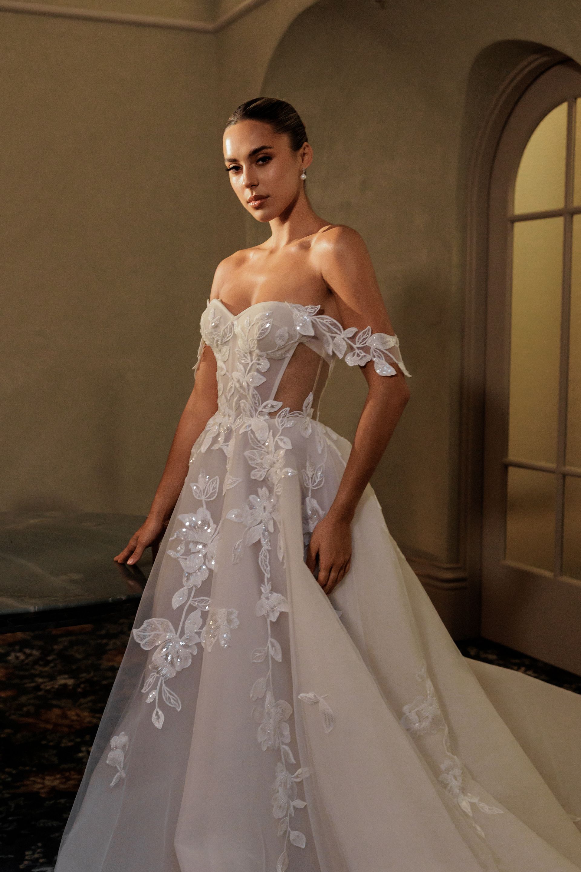 A woman in a wedding dress is standing in front of a window.