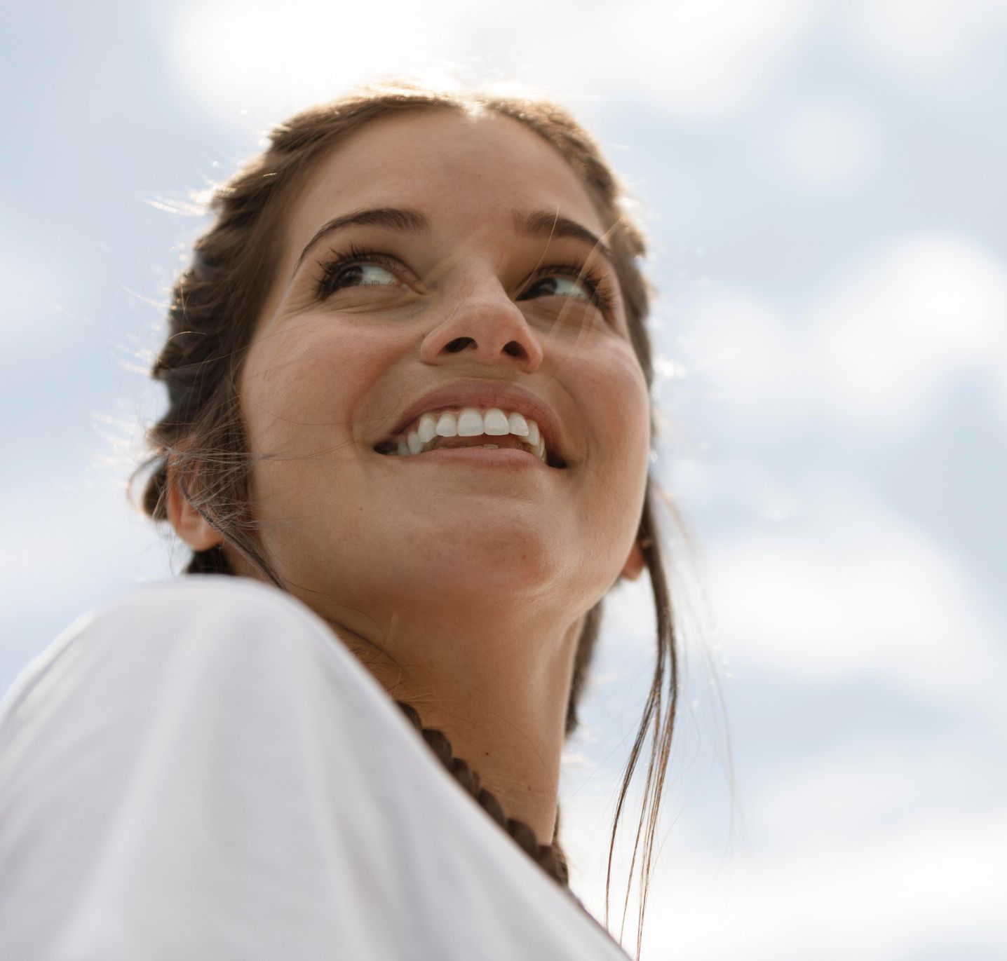 Woman looking up smiling against a blue and cloudy sky.