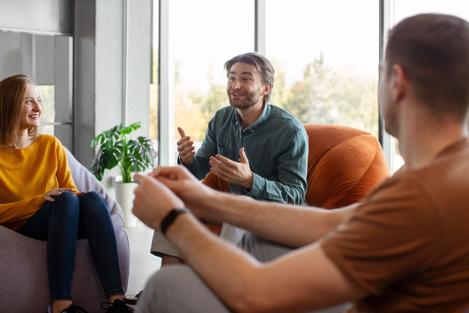 Therapist and couple in therapy session, seated in a room. The therapist gestures while speaking.