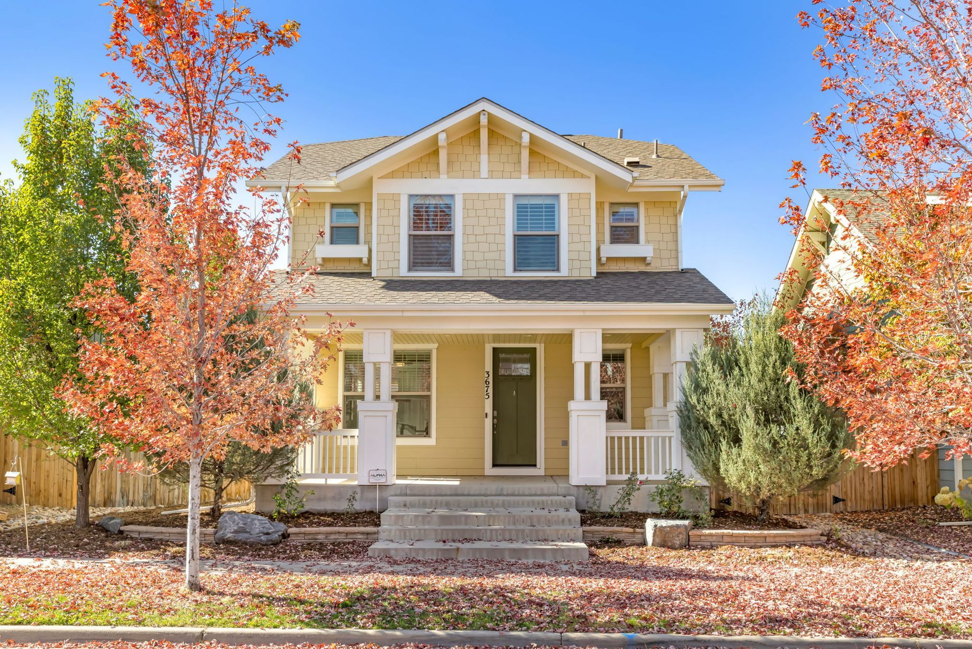 A yellow house with a porch and trees in front of it