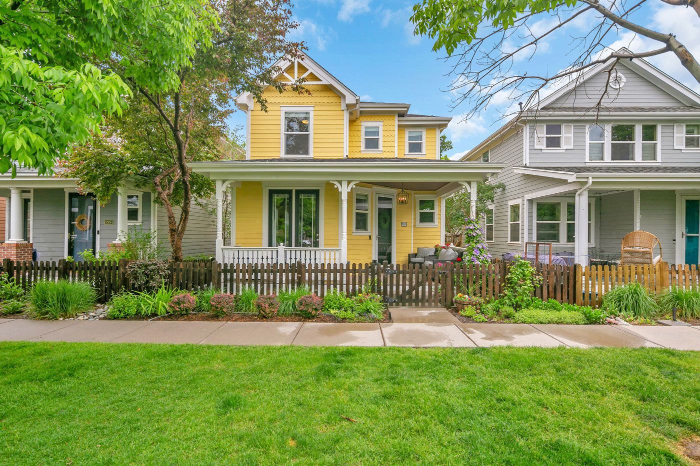 A yellow house with a porch and a fence in front of it.