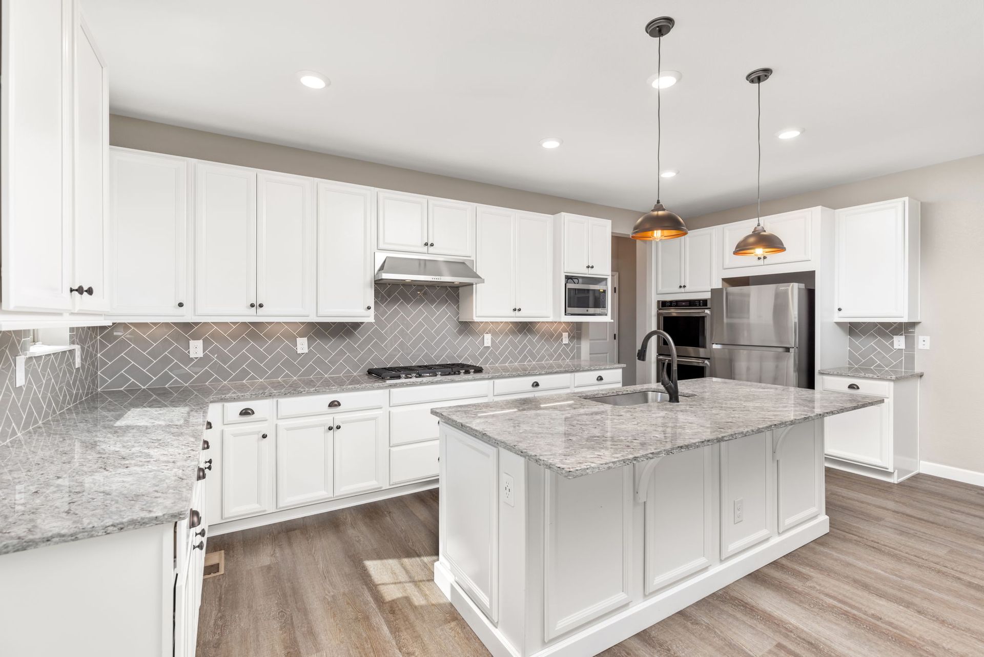 An empty living room with hardwood floors and a kitchen in the background.