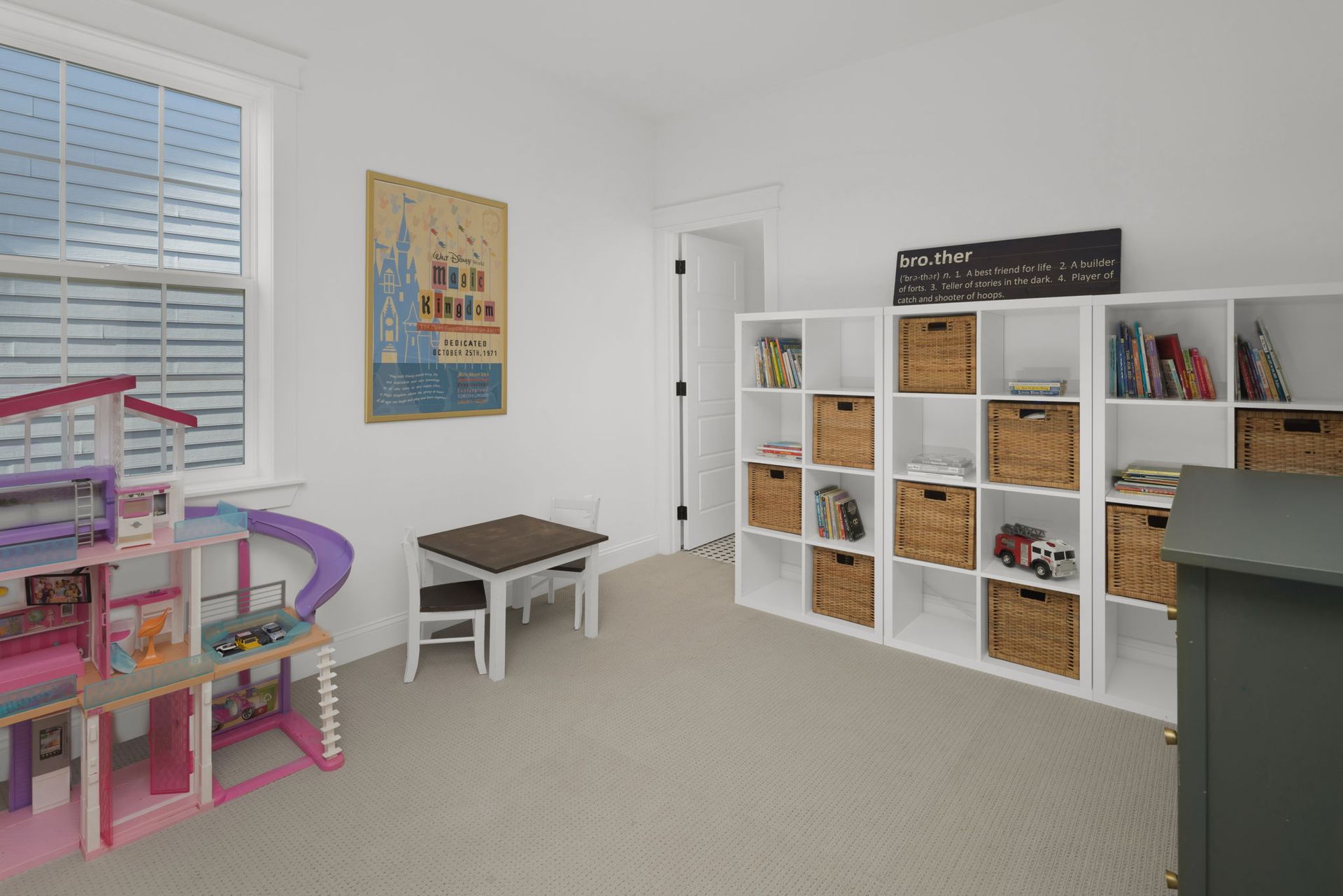 A play room with a table , chairs , shelves and a doll house.