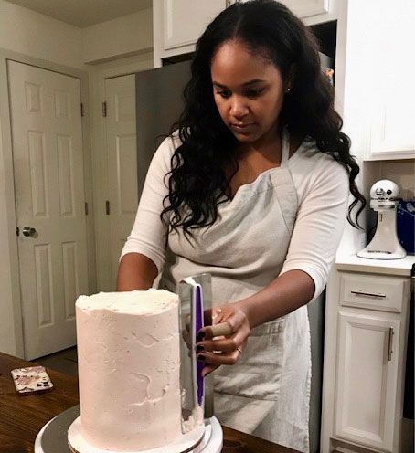 Woman smoothing frosting on a cake with a scraper in a kitchen.