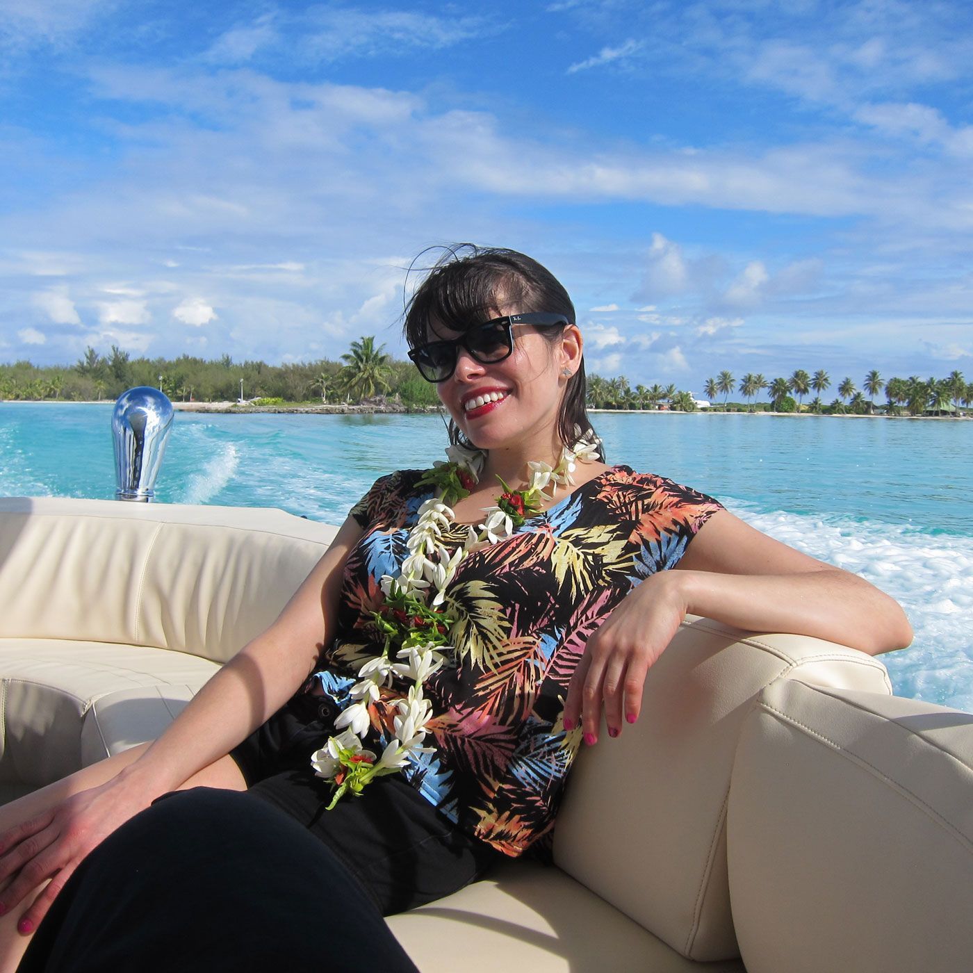 A woman wearing sunglasses is sitting on a boat in the water