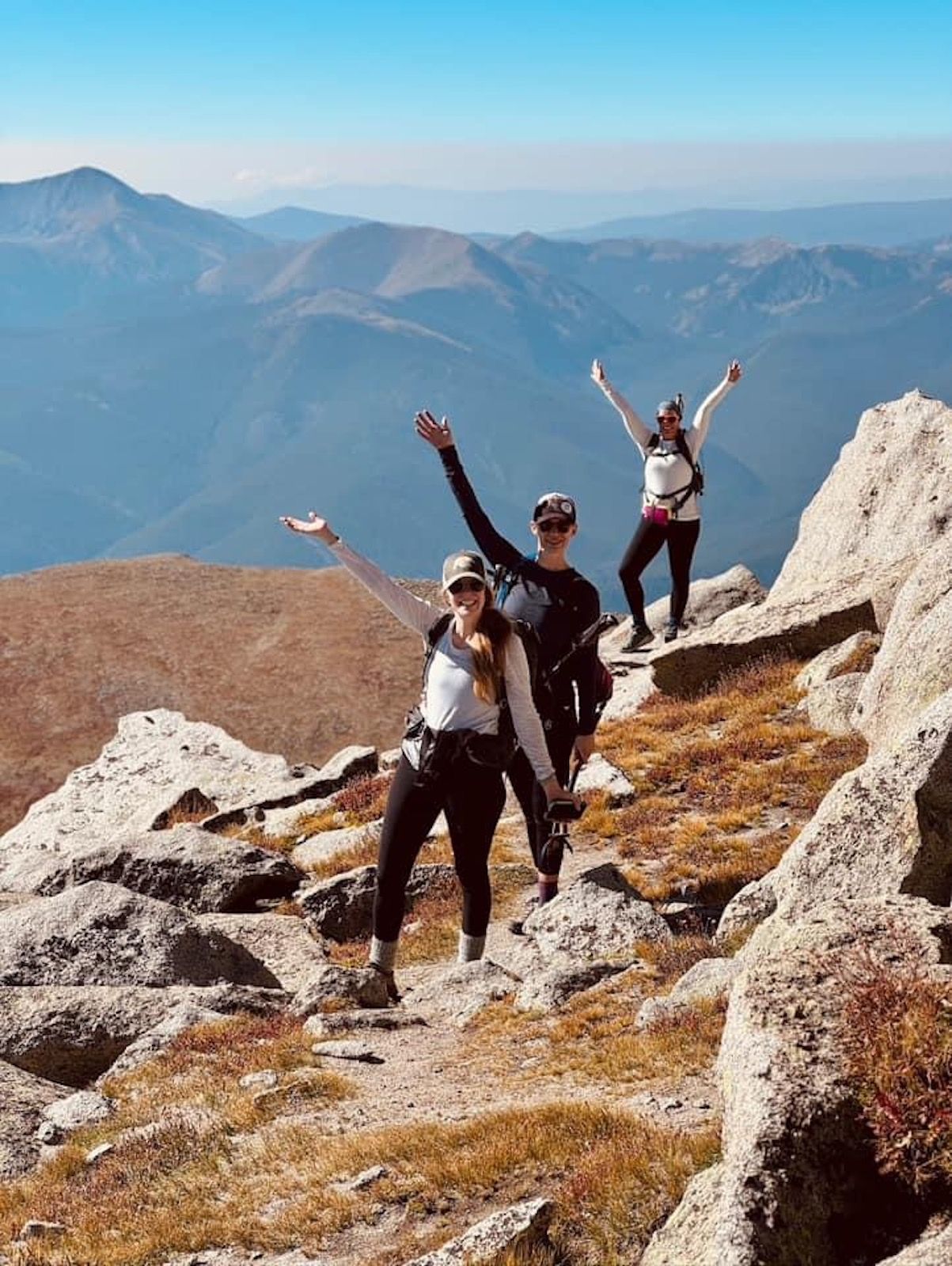 A group of people are standing on top of a mountain with their arms in the air.