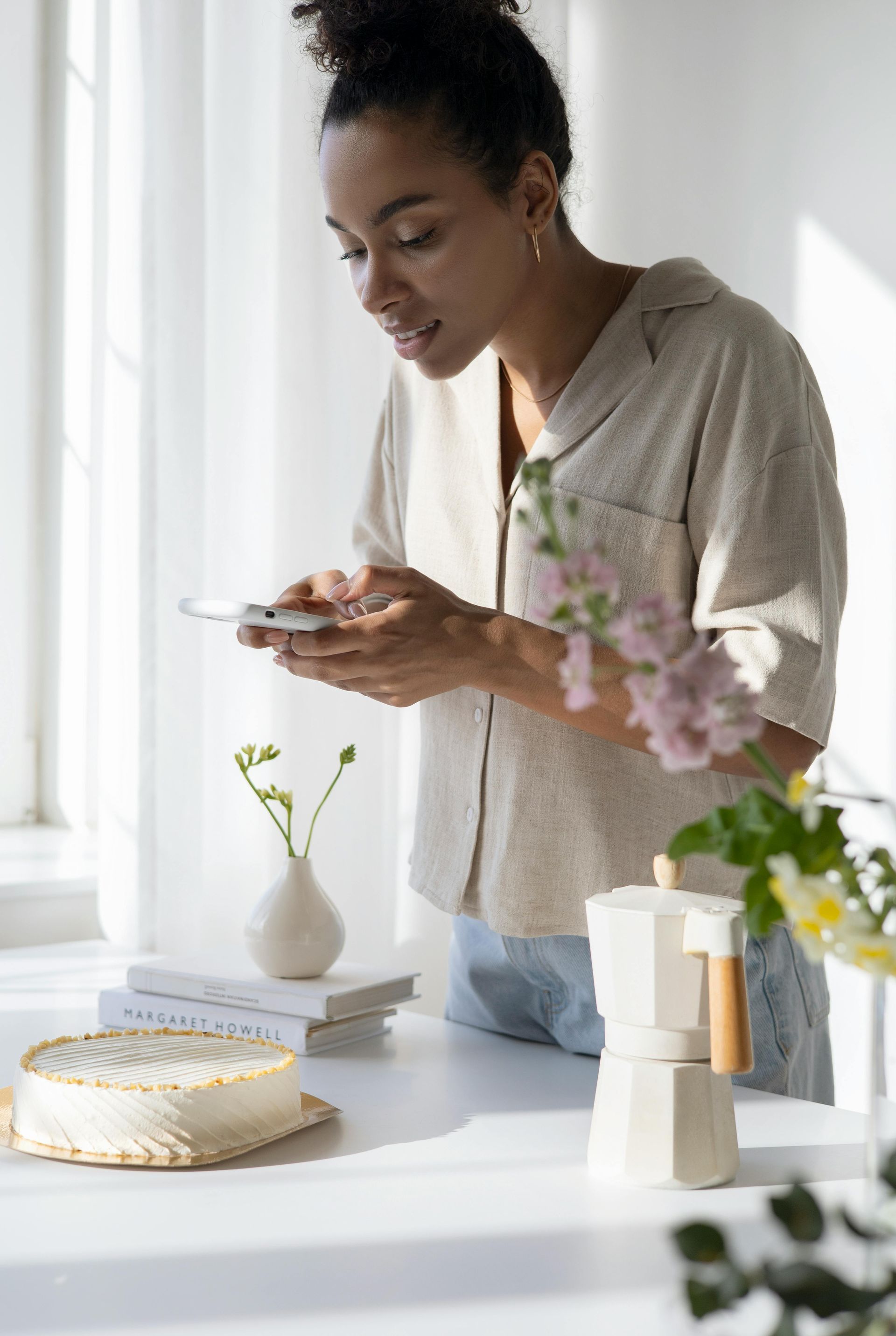 A woman is standing at a table looking at her phone.