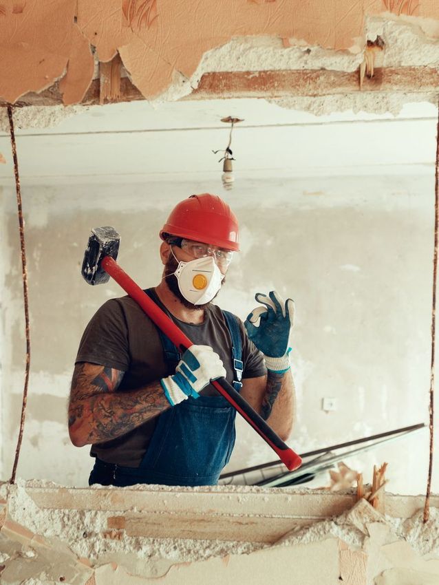 A man wearing a hard hat and a mask is holding a hammer.