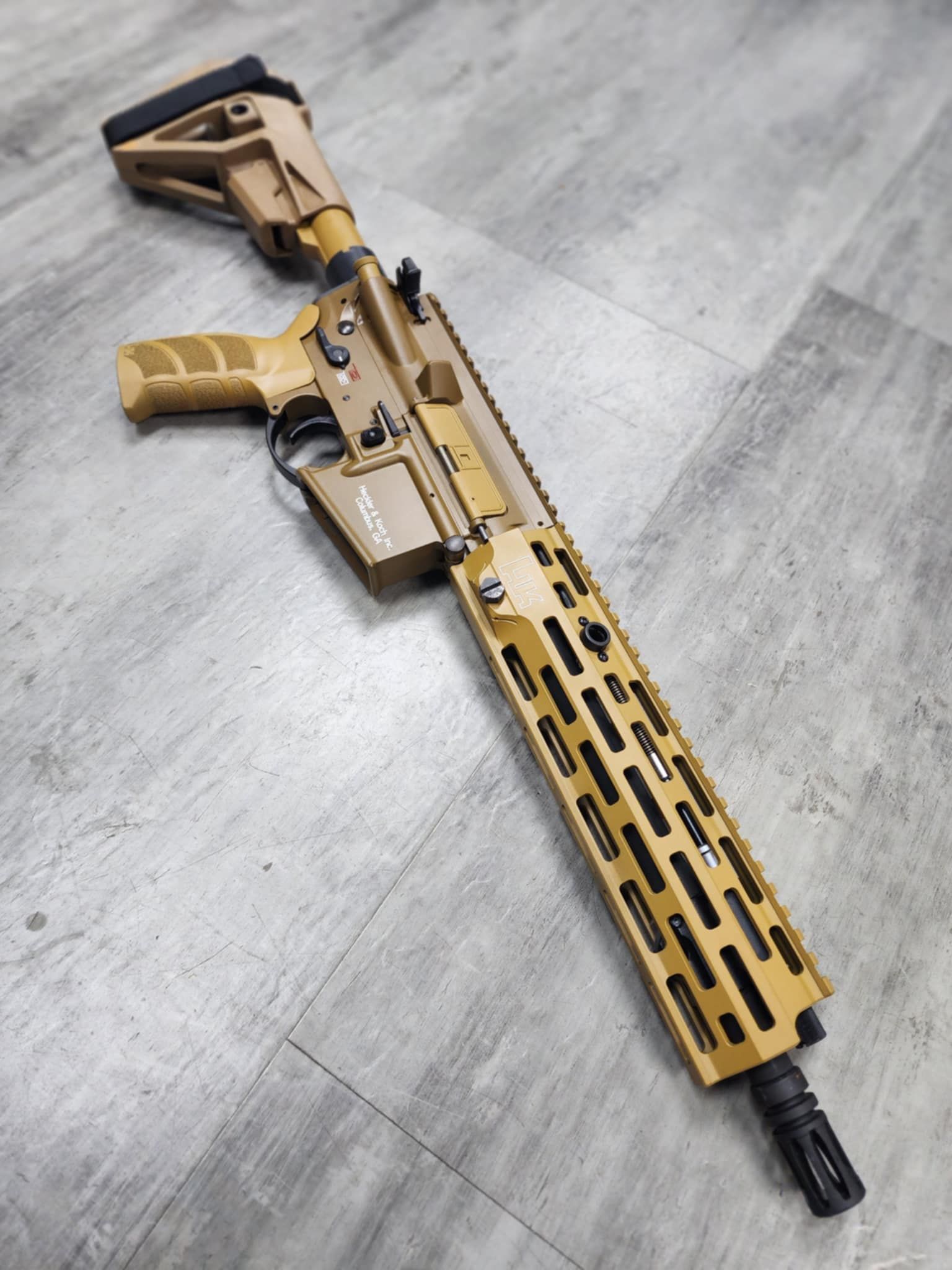Tan and black rifle on a gray wooden surface.