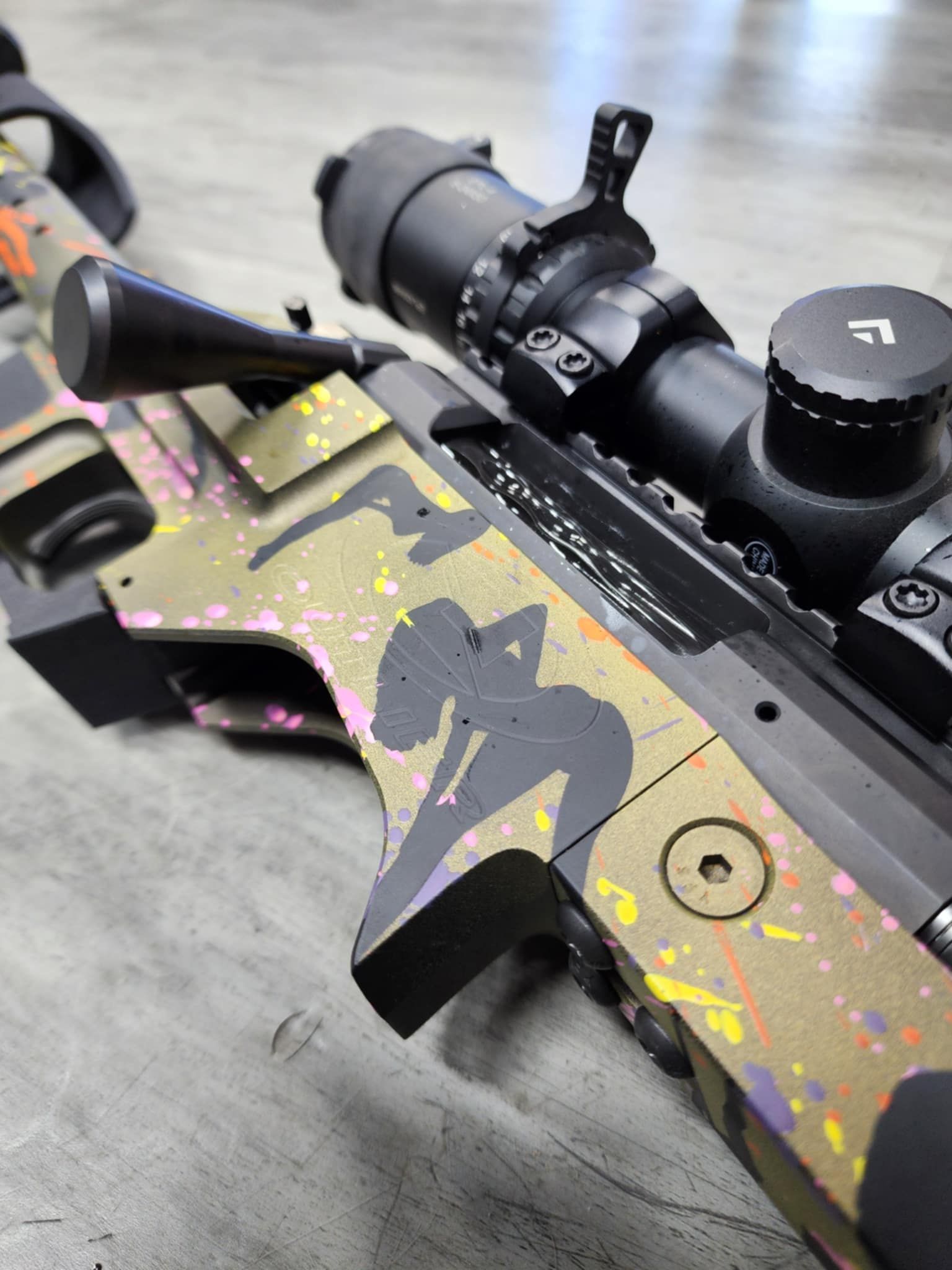 Custom painted rifle with scope, a nude figure stencil, and multi-colored splatters.
