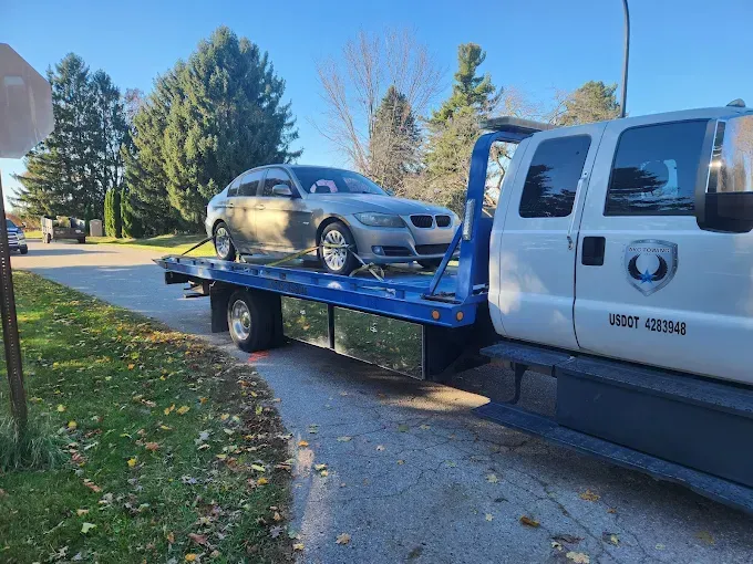 Silver BMW sedan on blue tow truck bed, roadside, sunny day.