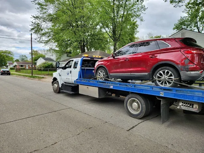 Red SUV being towed on a flatbed truck down a residential street.