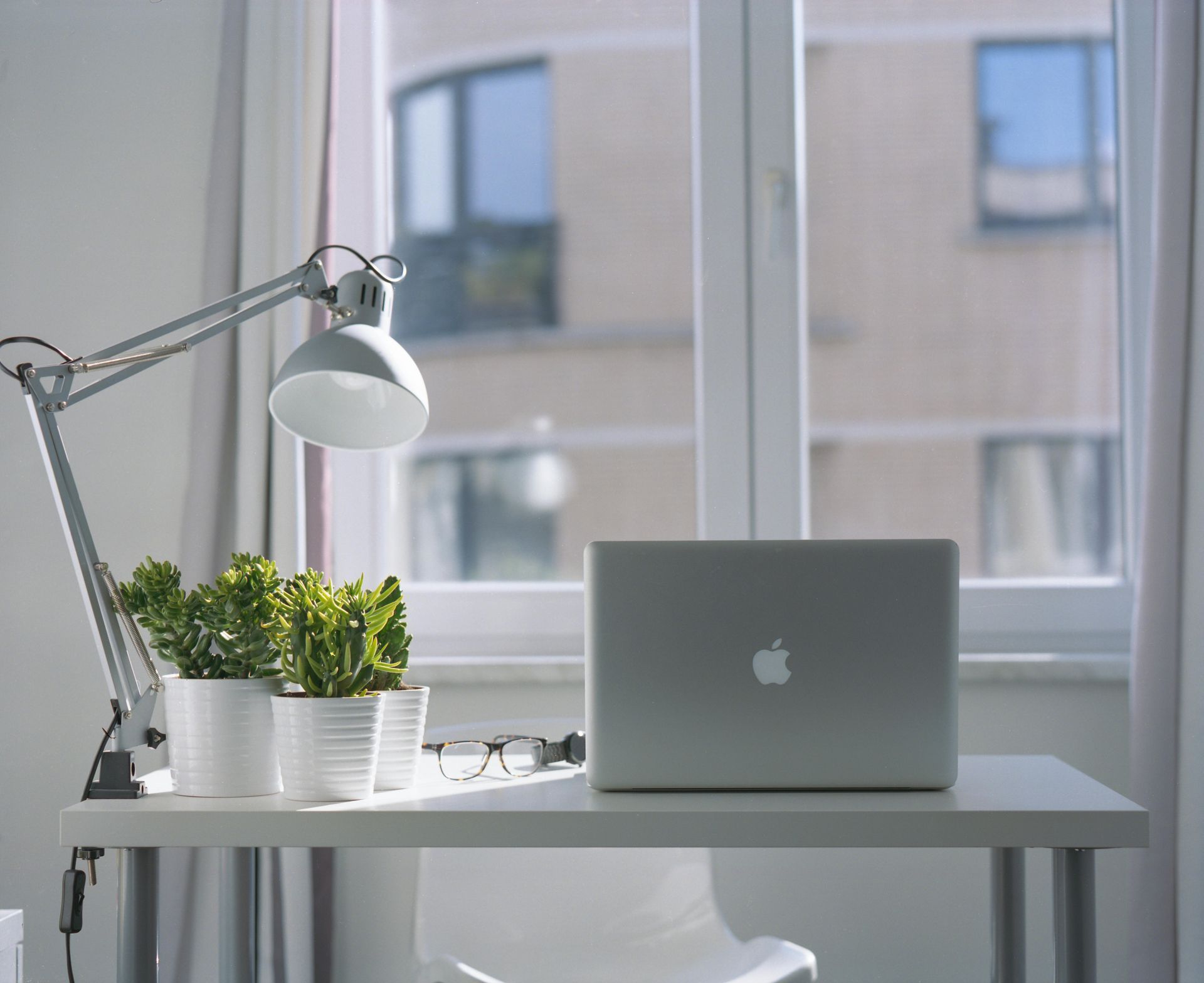 A laptop computer is sitting on a desk in front of a window.
