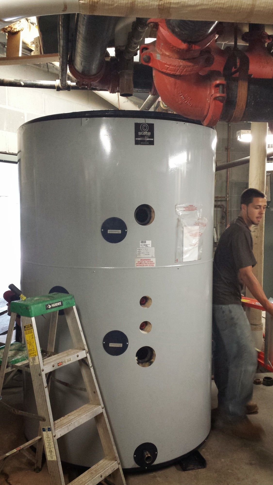 A man is standing next to a large white tank in a room.