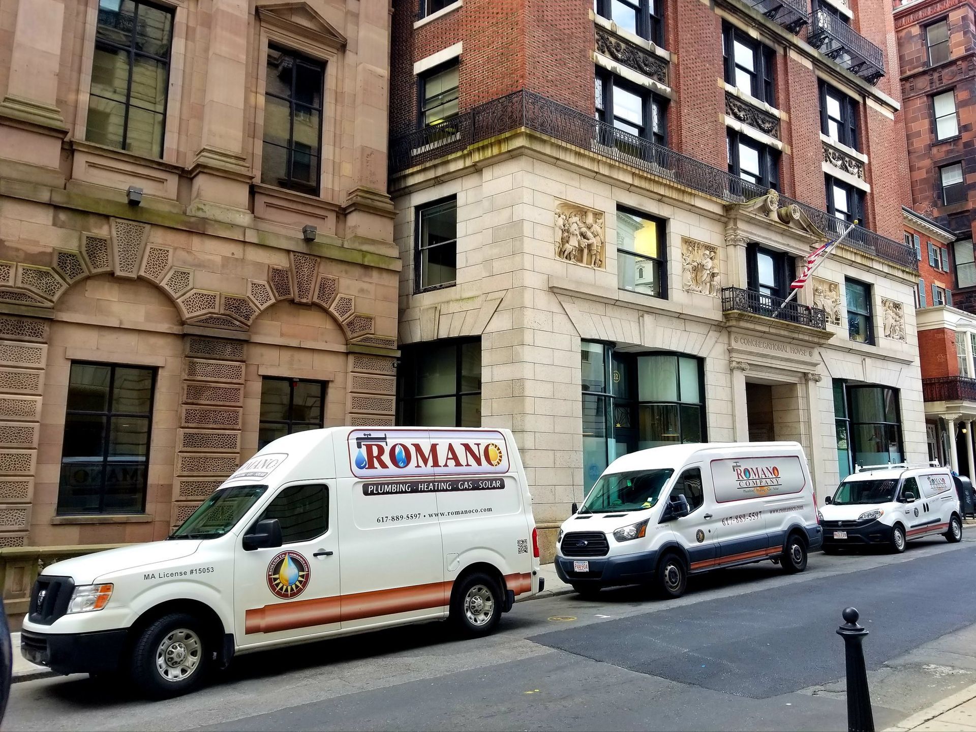 Three white vans are parked on the side of the road in front of a building.