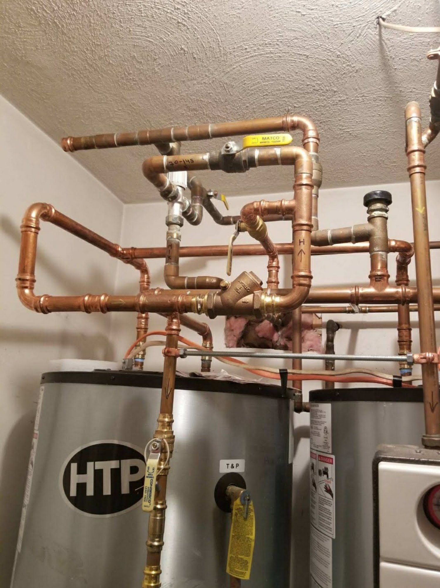 A htp water heater is surrounded by copper pipes