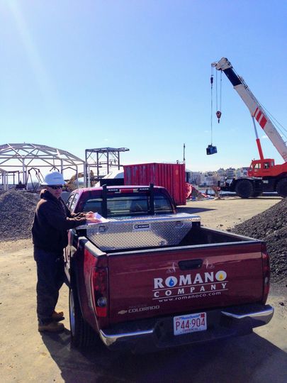 A man is standing next to a red truck that says romano company