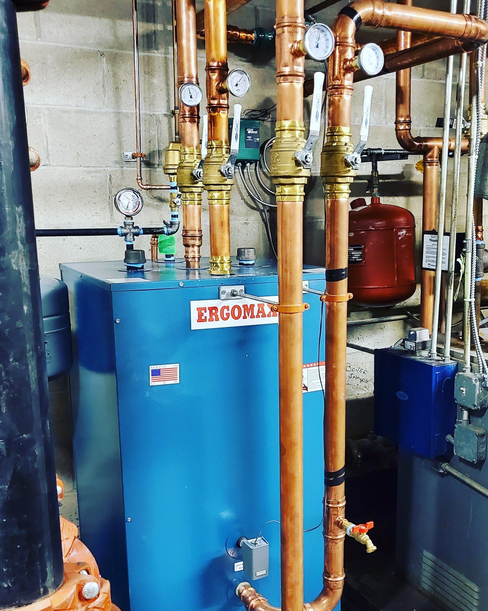 A blue ergomax water heater is surrounded by copper pipes