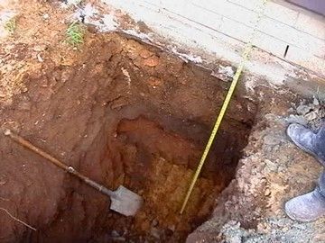 A person is measuring a hole in the ground with a tape measure.