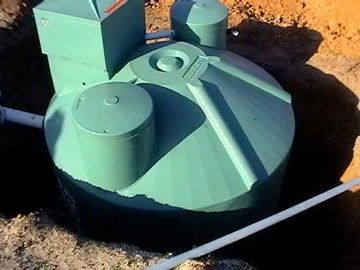 A green septic tank is sitting in the dirt next to a pipe.