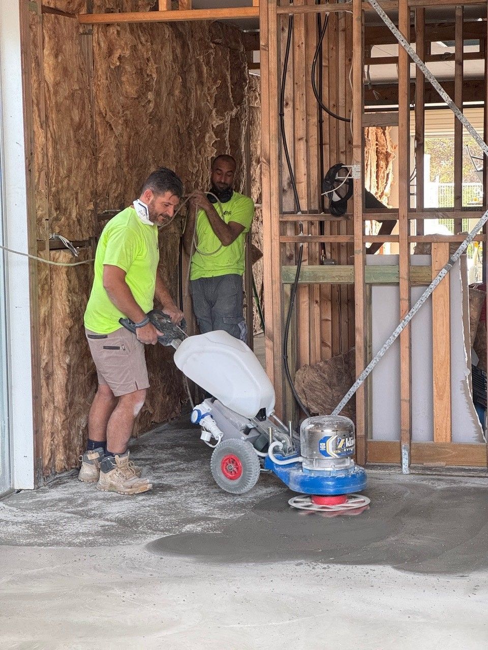 A man is using a machine to polish the floor of a building under construction.
