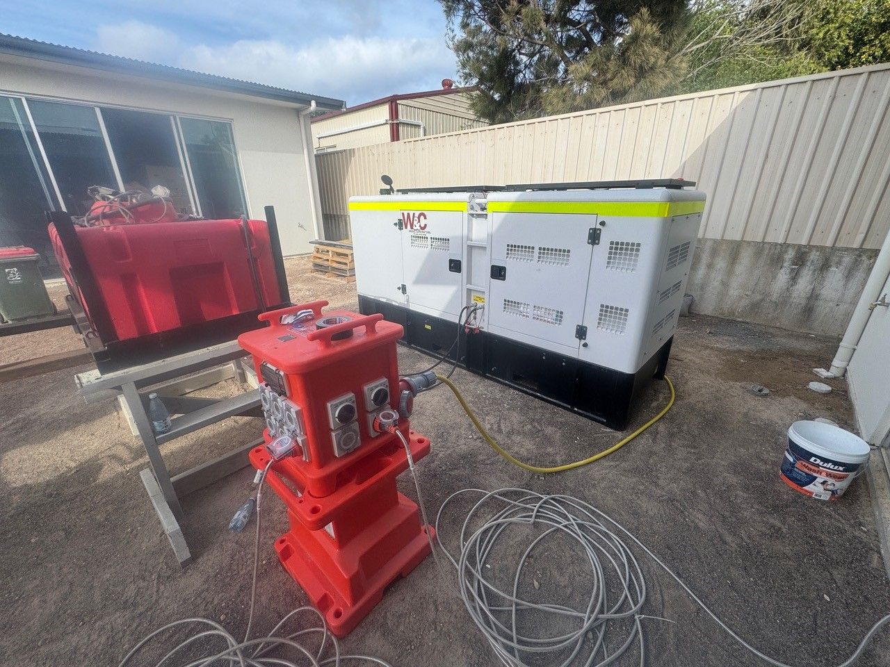 A generator is sitting on the ground next to a bucket of paint.