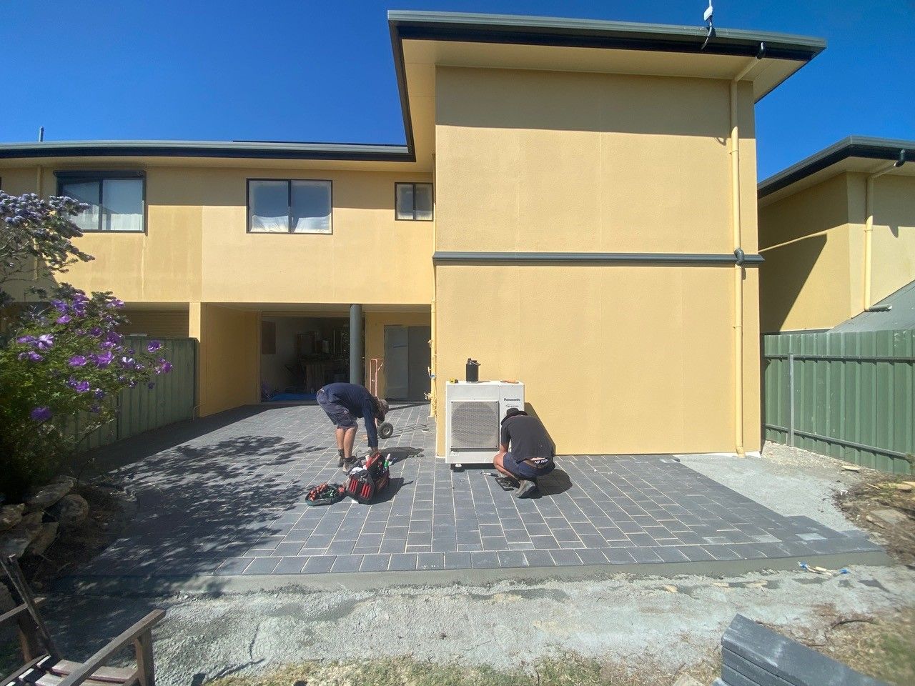Two men are working on a patio in front of a house.