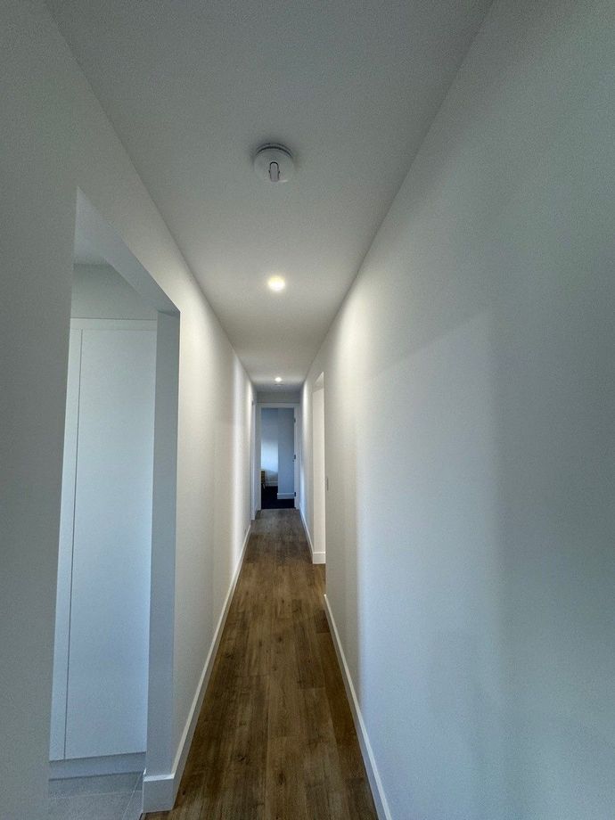 A long hallway with white walls and wooden floors in a house.