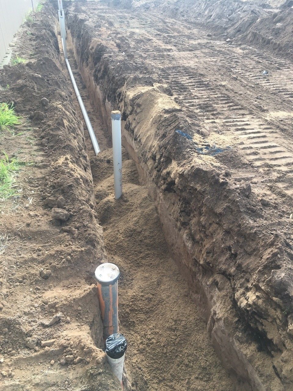 A drain pipe is being installed in a trench in the dirt.