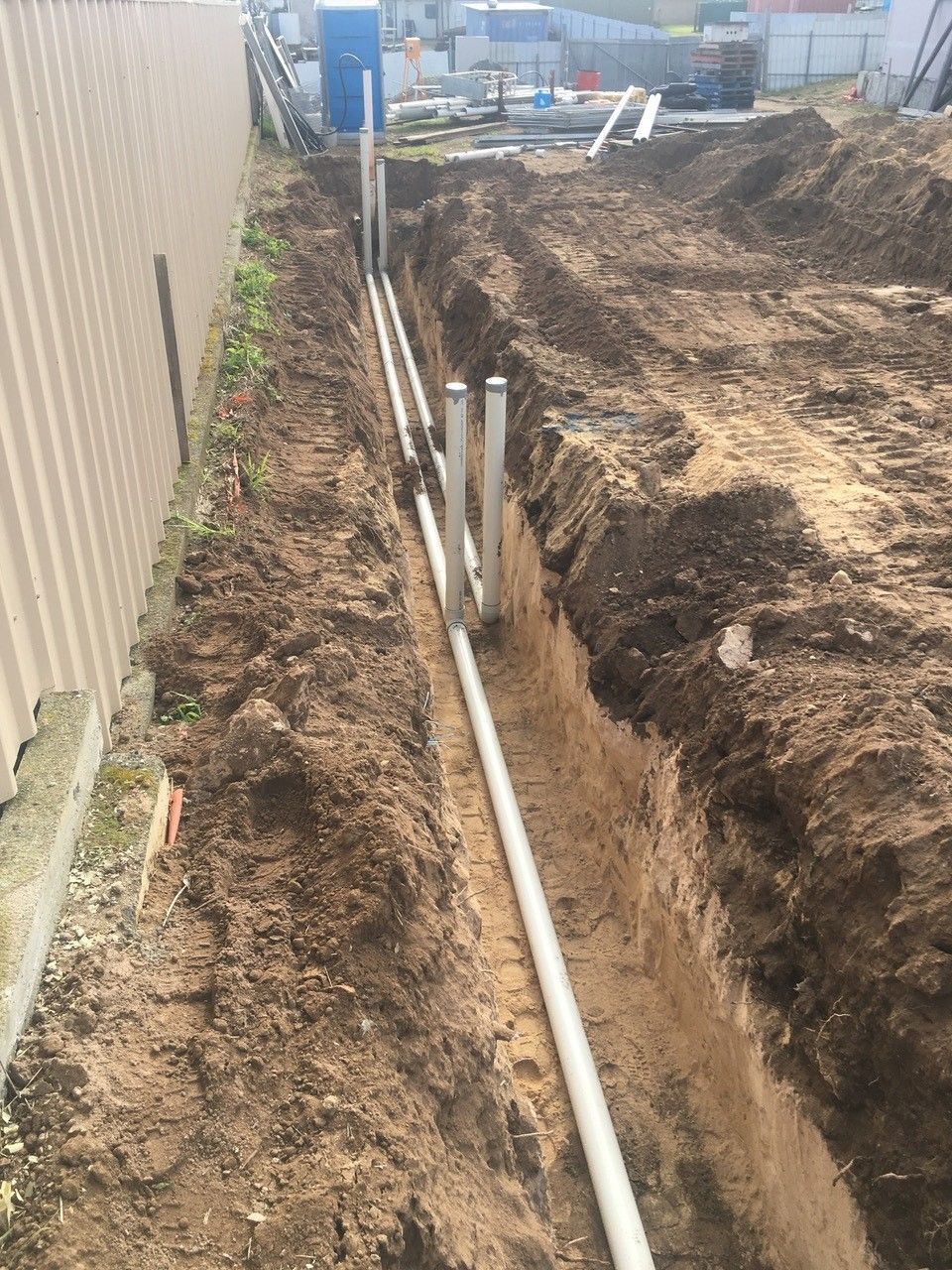 A bunch of pipes are laying in the dirt in a trench.