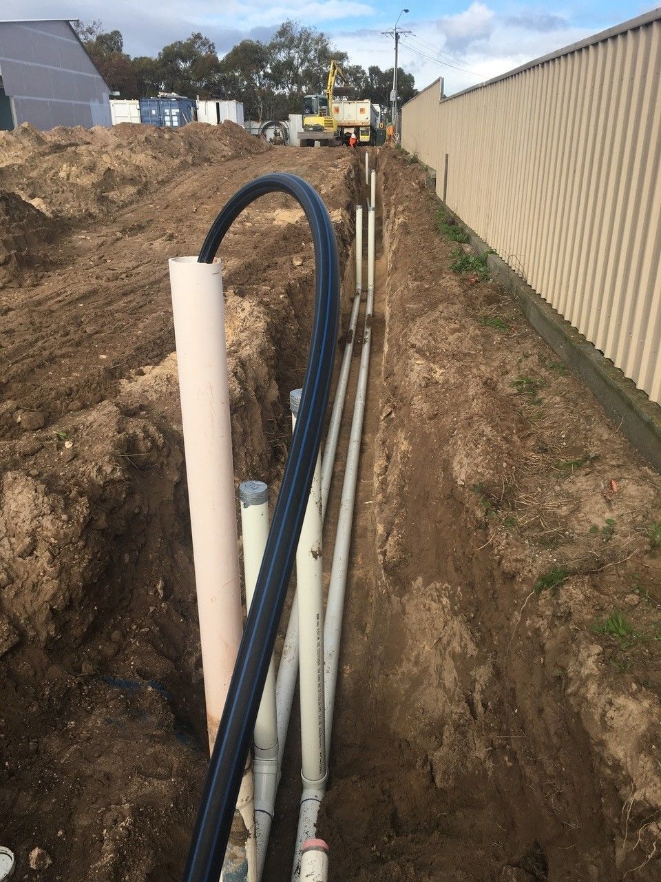A row of pipes are being installed in a trench next to a fence.
