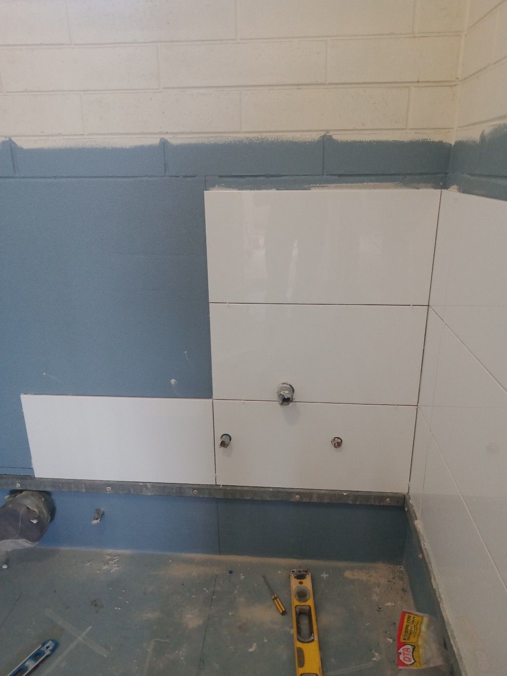 A bathroom with blue and white tiles being installed and a level on the floor.