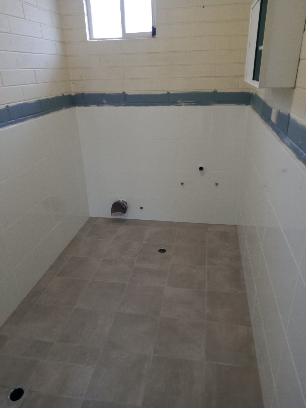 An empty bathroom with white tiles and a window.