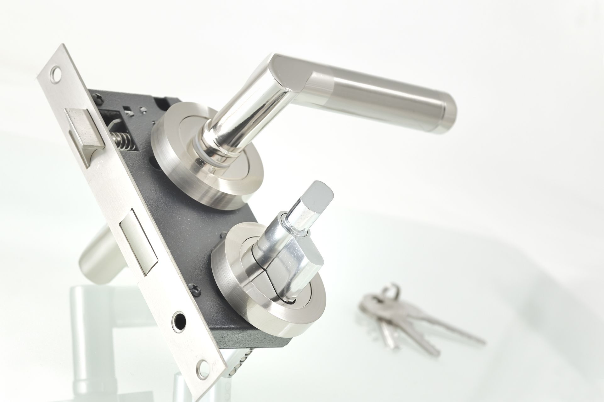 Maniglia per porta color argento con meccanismo di chiusura e chiavi su sfondo bianco.
