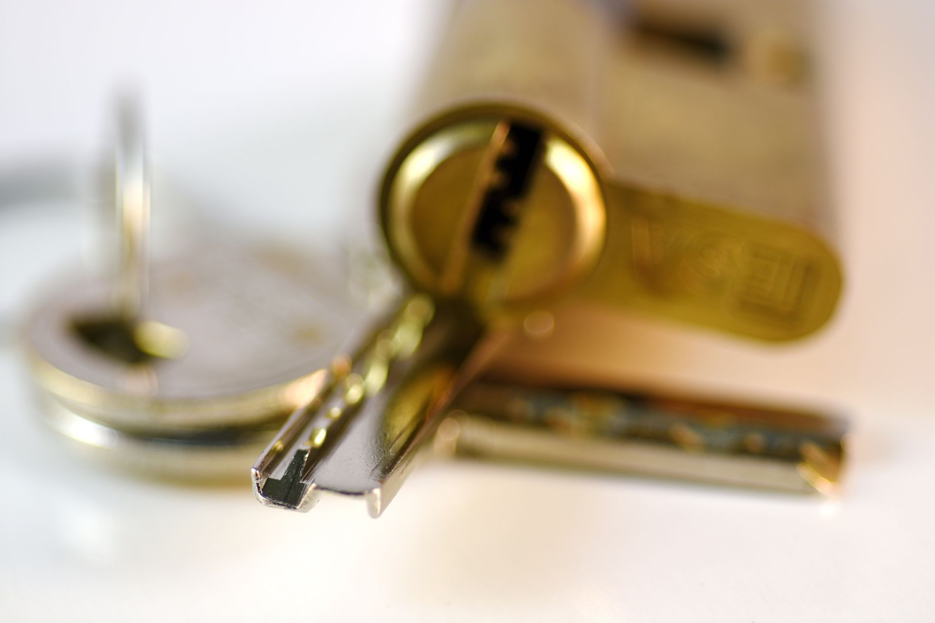 In primo piano una chiave metallica, mentre sullo sfondo si intravede un cilindro di serratura in ottone leggermente sfocato.