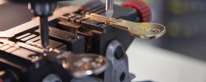 Primo piano di una macchina duplicatrice di chiavi in metallo con struttura arancione e blu scuro, che mostra una chiave tenuta in una morsa metallica.