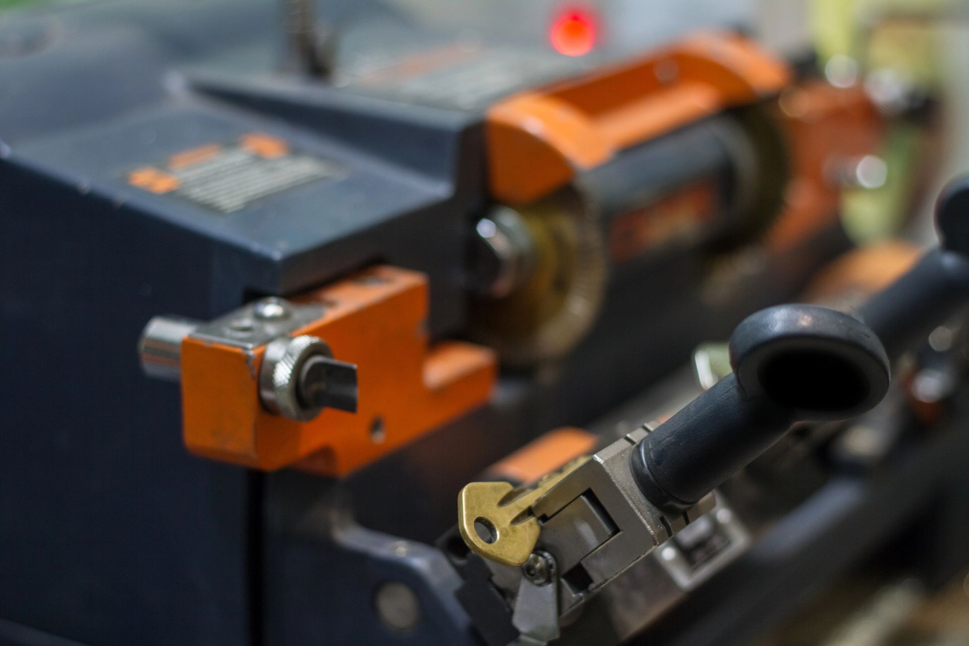 Primo piano di una macchina duplicatrice di chiavi in ​​metallo con struttura arancione e blu scuro, che mostra una chiave tenuta in una morsa metallica.