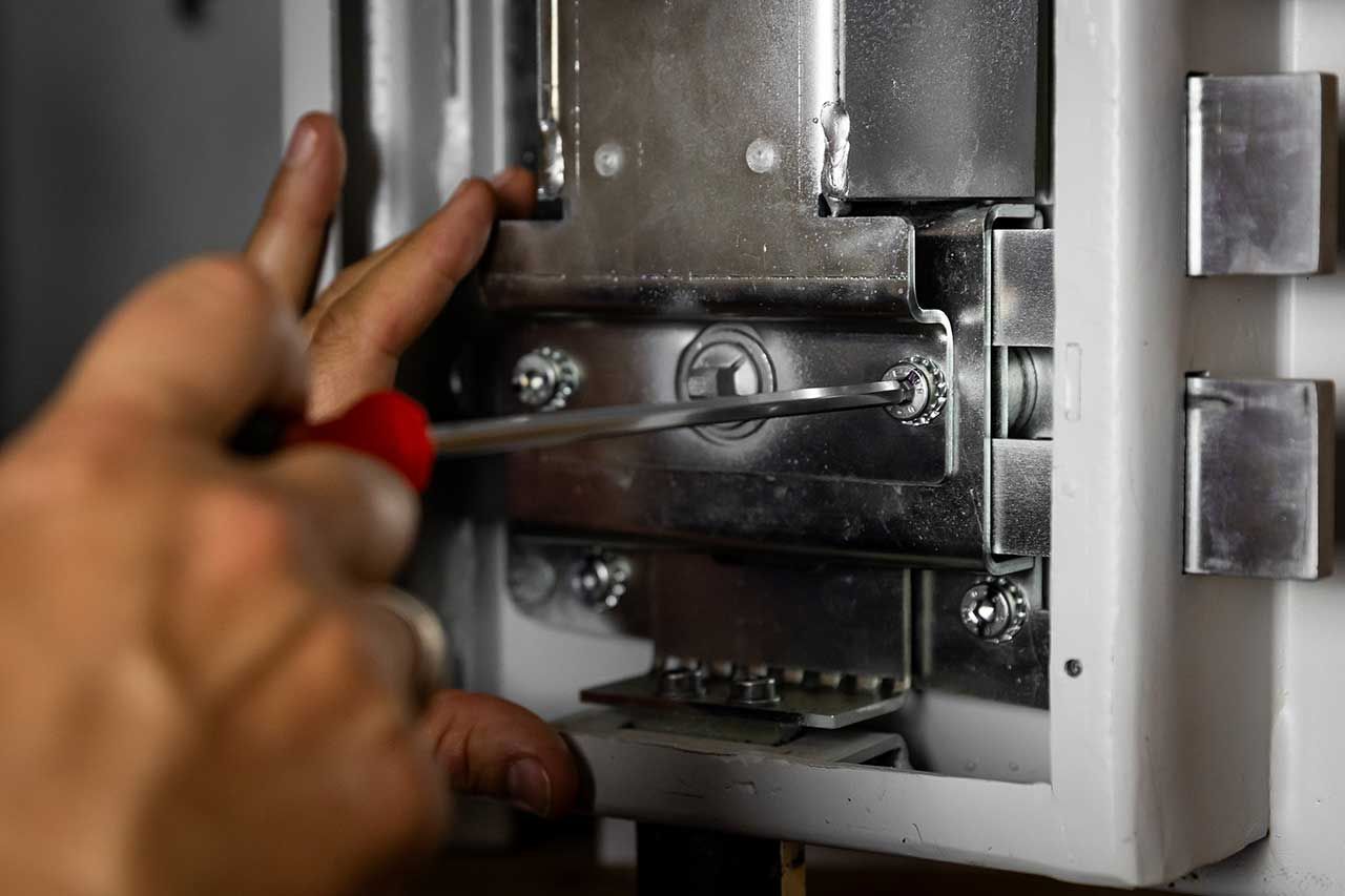 Primo piano di mani che usano un cacciavite per stringere un bullone metallico su un meccanismo di chiusura all'interno di un telaio di una porta bianca.