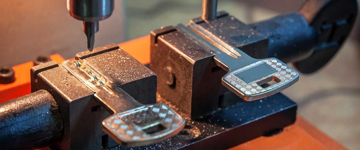 Una macchina duplicatrice di chiavi che riproduce una chiave metallica con una fresa, generando trucioli metallici sulla superficie di lavoro.