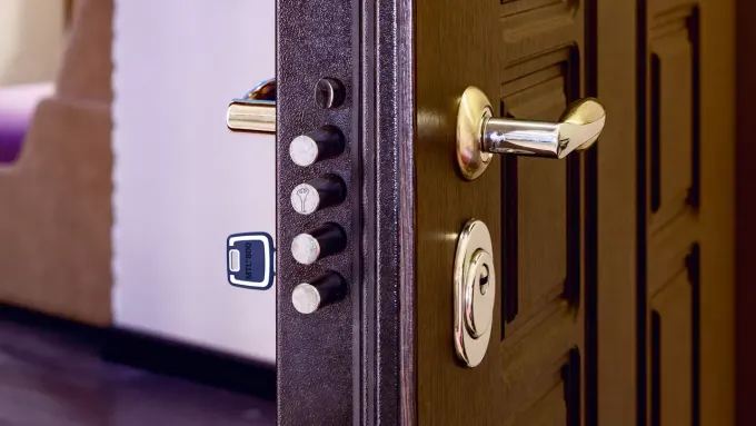 Una mano usa un cacciavite per stringere una vite sul meccanismo di chiusura di una porta, vicino a un portachiavi.