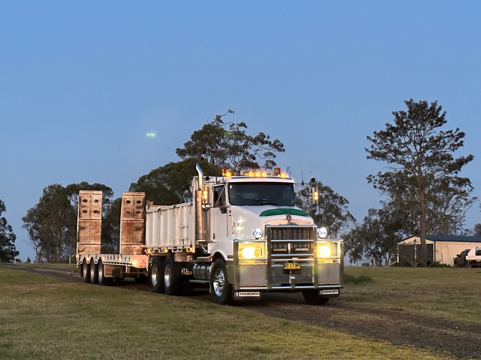 A White Semi-truck With a Flatbed Trailer Driving on Grass — PVM Contracting in Alstonville, NSW