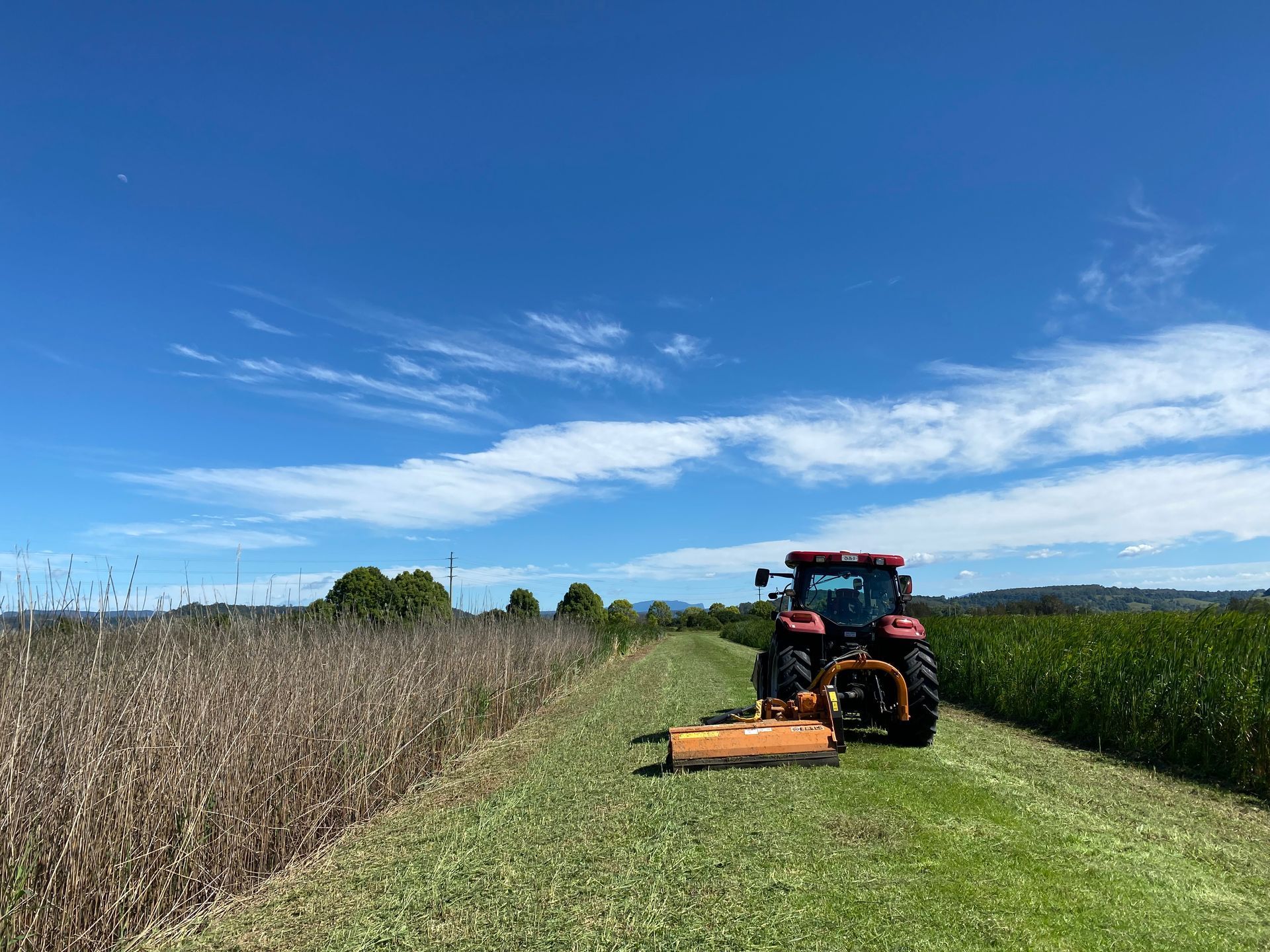 A Red Tractor With an Orange Mower Cuts Grass — PVM Contracting in Alstonville, NSW