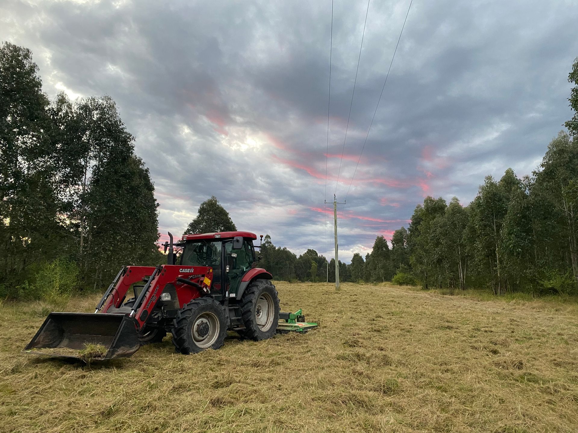 A Red Tractor With a Front Loader is Parked in a Field — PVM Contracting in Yamba, NSW